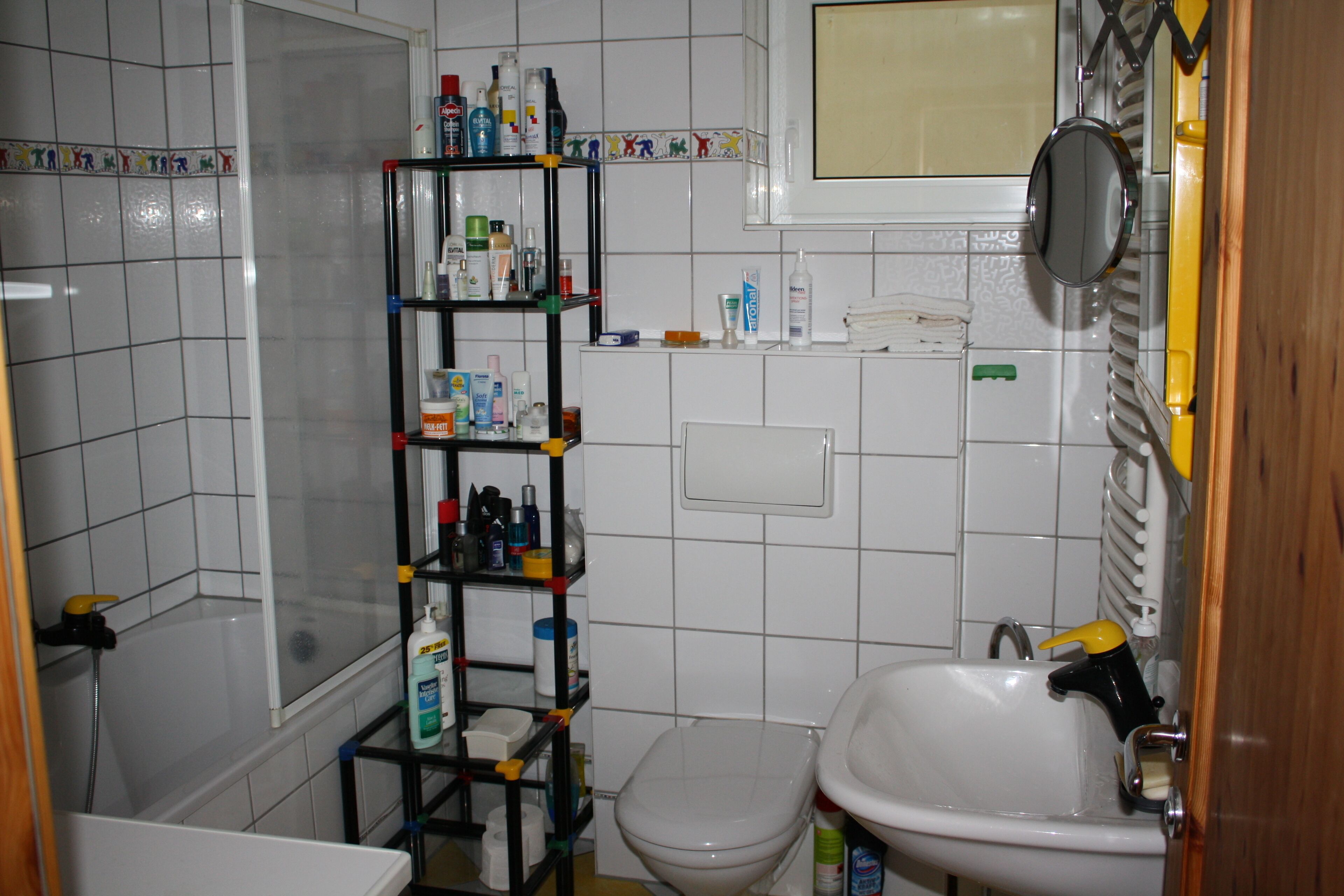A bathroom with a toilet, sink, and shelves with toiletries.