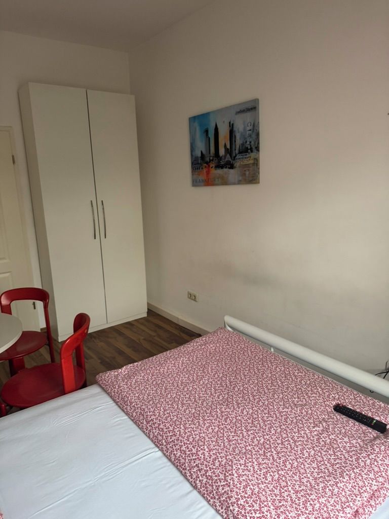 Ein Schlafzimmer mit einem Bett, einem roten Sessel, einem Kleiderschrank und einem Bild an der Wand.