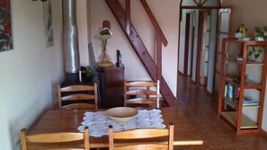 A dining area with a wooden table, chairs, and a lace table runner. A staircase leads to another room.