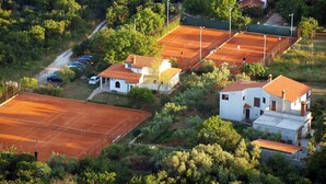An aerial view of a residential area with multiple houses, a tennis court, and surrounding greenery.