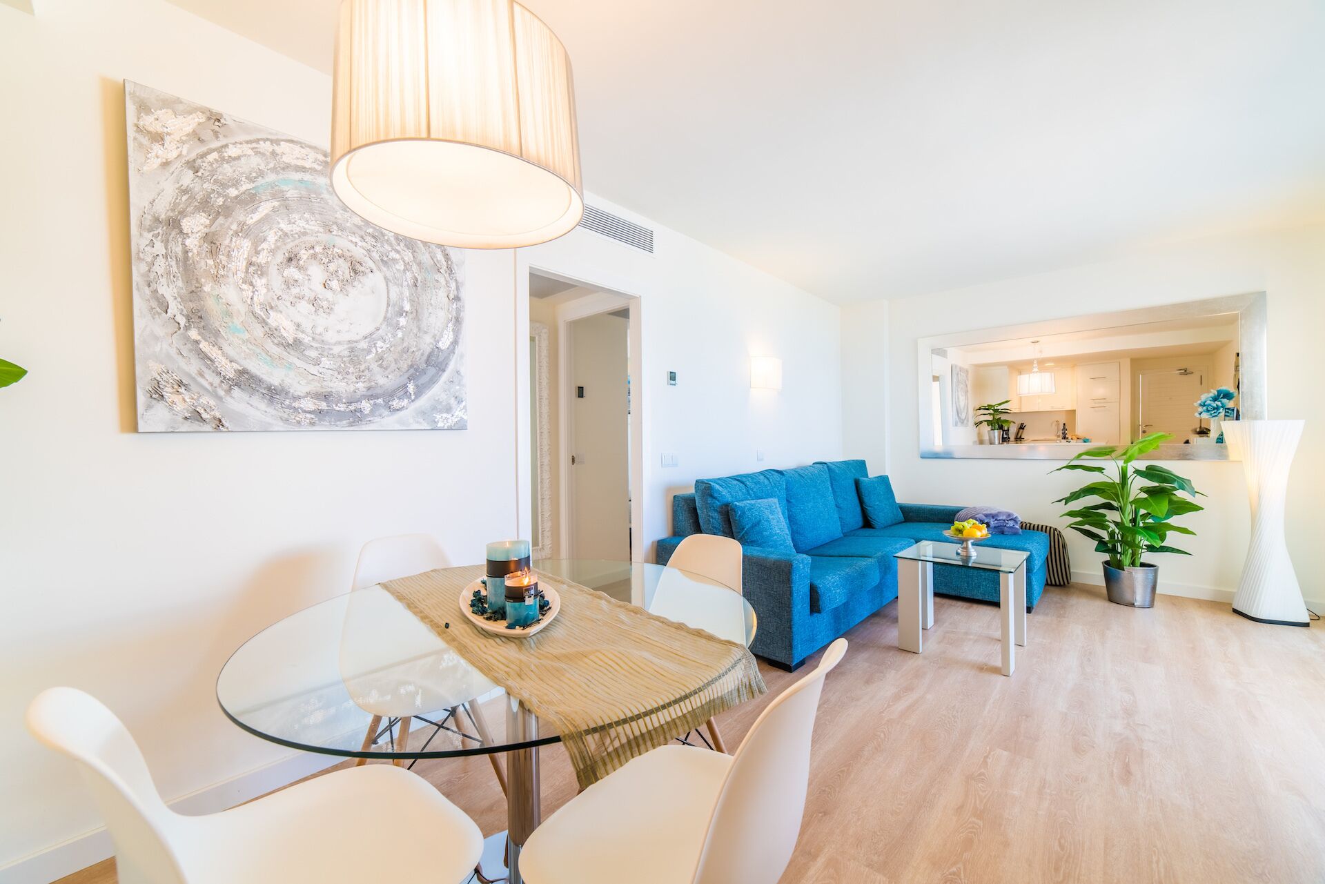 Ein modernes Wohnzimmer mit einem Glastisch, einem blauen Sofa und einem großen abstrakten Gemälde an der Wand.
