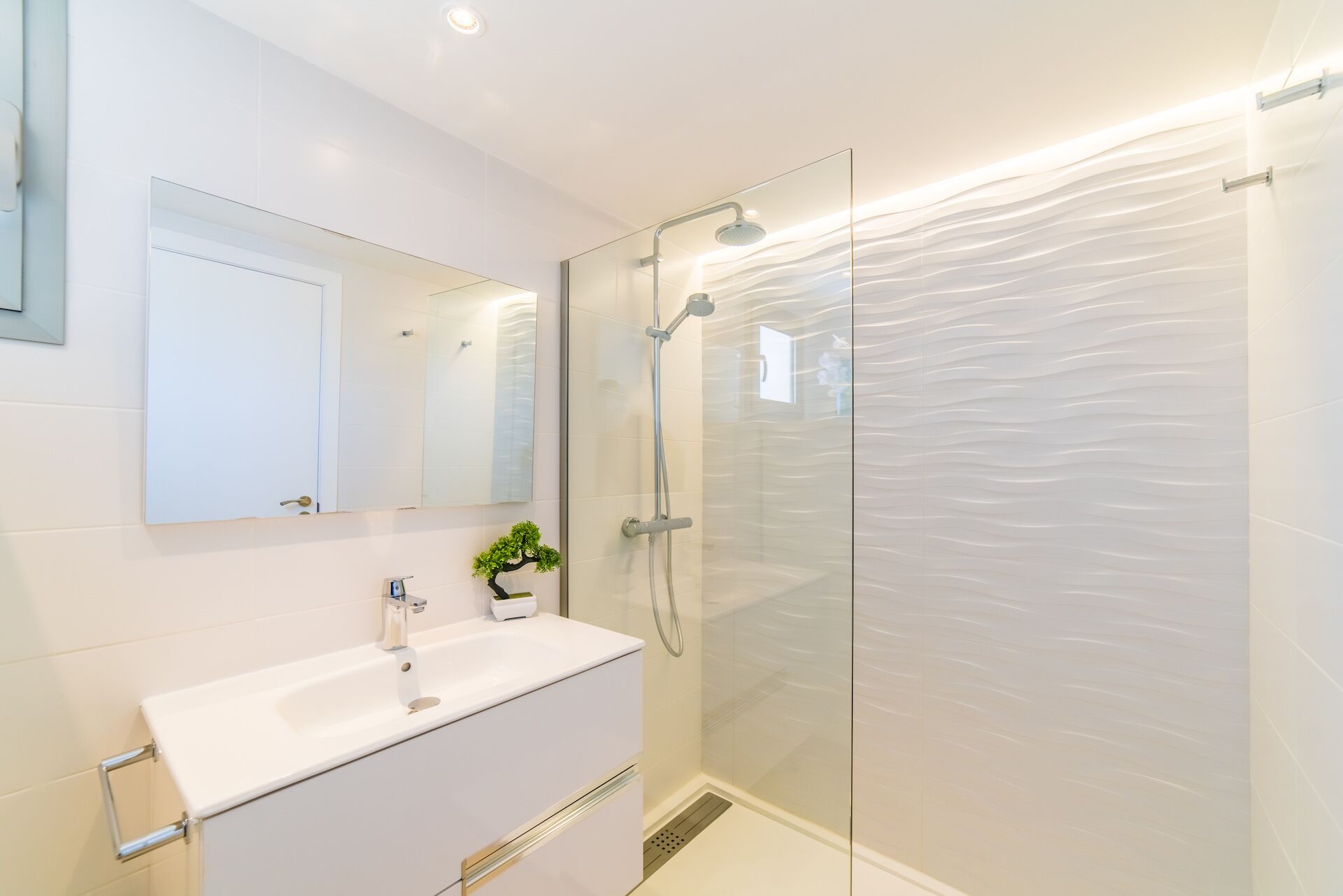 A modern bathroom with a glass shower enclosure, a white vanity with a sink, and a small potted plant.