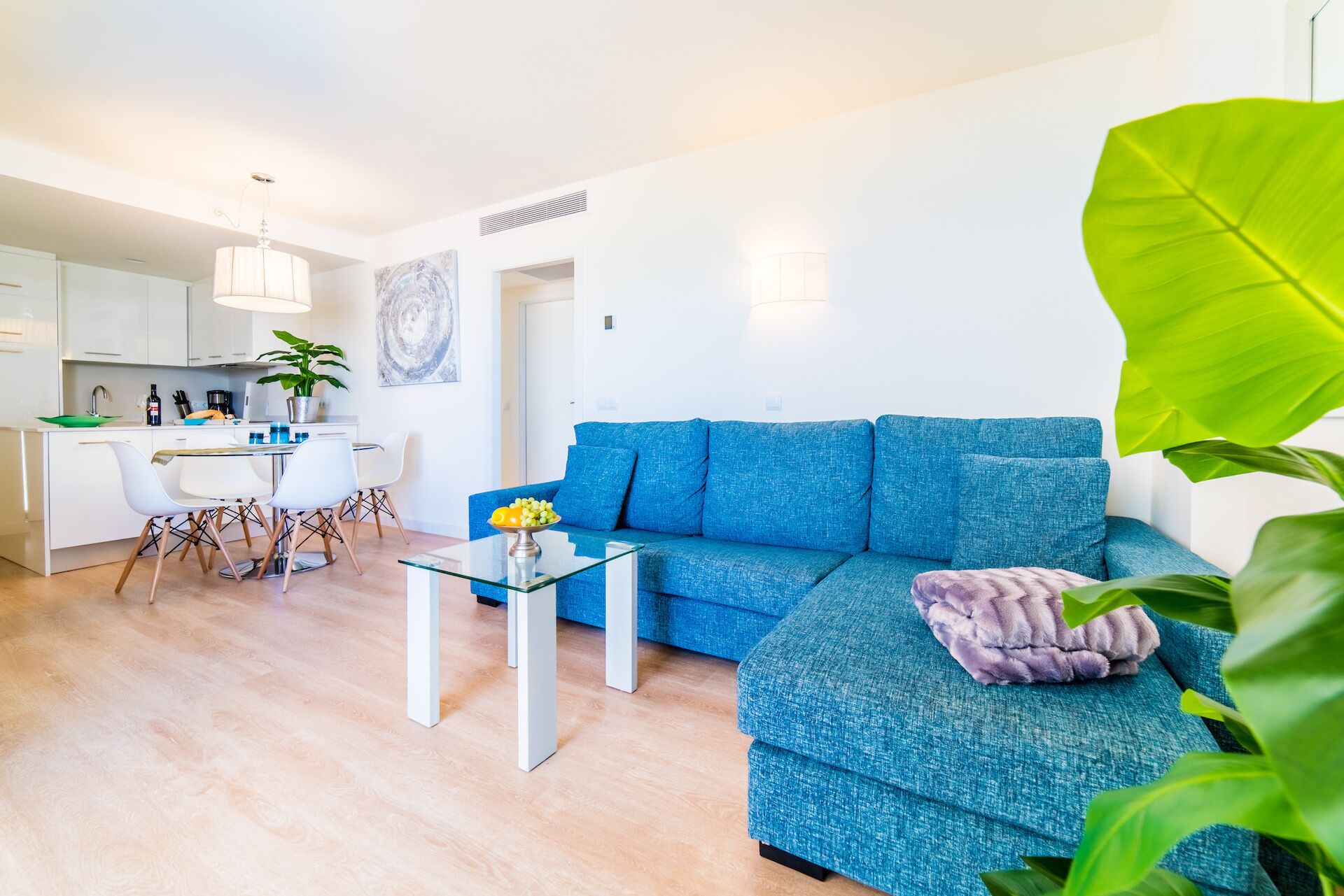Un salon moderne avec un canapé bleu, une table basse en verre et un coin repas avec des chaises blanches.