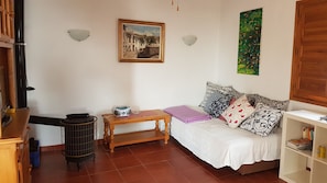 A cozy room with a bed, a small table, a radiator, and a wall with a painting and a green artwork. - Small house with pool in the olive grove with sea view (Iznate)
