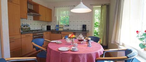 A dining area with a round table covered by a pink tablecloth, surrounded by blue chairs. A white pendant light hangs above the table.