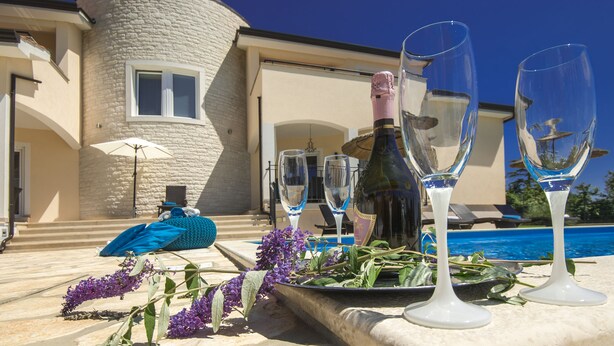 Une scène de bord de piscine avec une bouteille de champagne, des verres et des fleurs disposés sur une table.