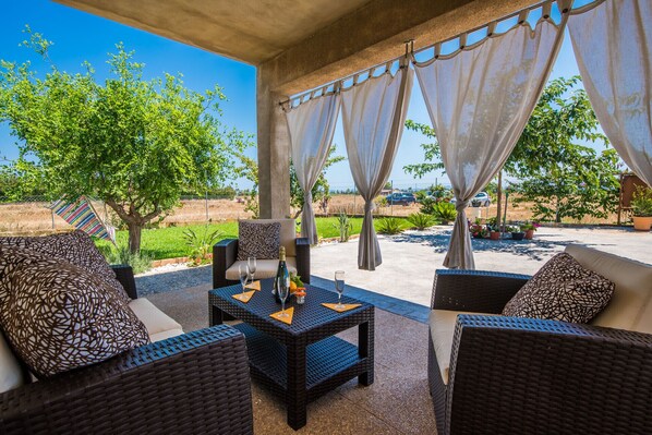 An outdoor seating area with wicker furniture, a table with wine glasses, and a view of a green landscape.