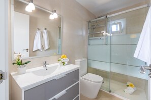 Ein modernes Badezimmer mit einer begehbaren Glasdusche, einem weißen Waschbecken mit Spiegel darüber und einer Toilette.