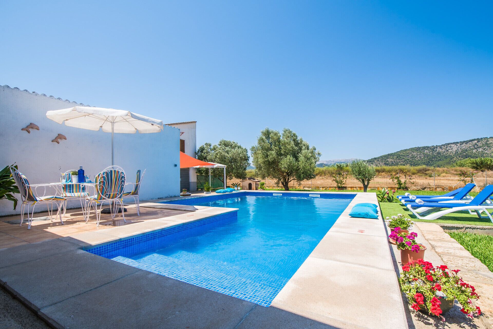 A swimming pool with a tiled edge, surrounded by lounge chairs and a table with chairs.
