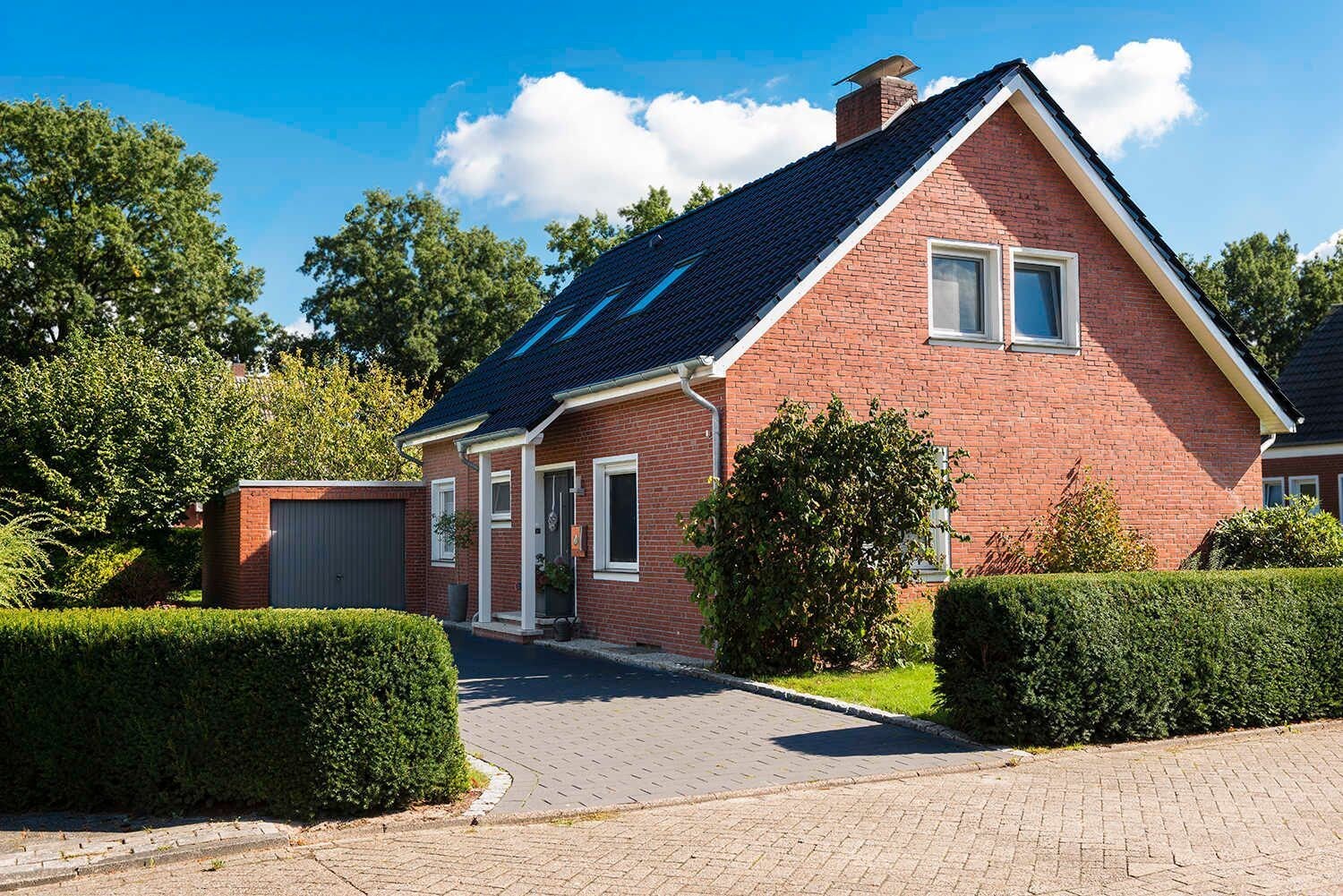 A two-story brick house with a sloped roof, a garage, and a well-maintained front yard with hedges.