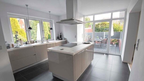 A modern kitchen with a central island, large windows, and a view of the outdoor patio area. - Feha - Holiday House "Minnet", 15169 (Leer (Ostfriesland))