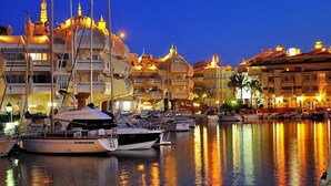 A marina with multiple yachts docked, surrounded by buildings with traditional architecture.
