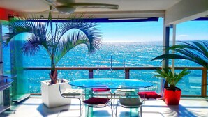 A modern room with a glass table, chairs, and a view of the ocean.