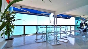 A modern, spacious balcony with a glass table and chairs, overlooking a body of water.