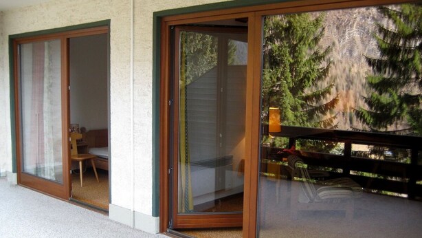 Une porte-fenêtre coulissante donnant sur un balcon avec vue sur les arbres et une terrasse en bois.