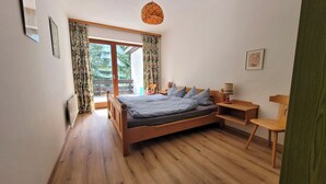 Une chambre à coucher avec un lit en bois, une table de chevet, une lampe et une vue sur l’extérieur grâce à une grande fenêtre.