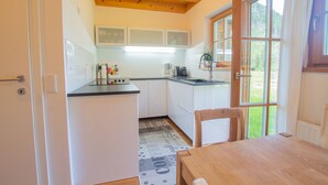 Una cocina pequeña con armarios blancos, techo de madera y ventana con vista a la vegetación.