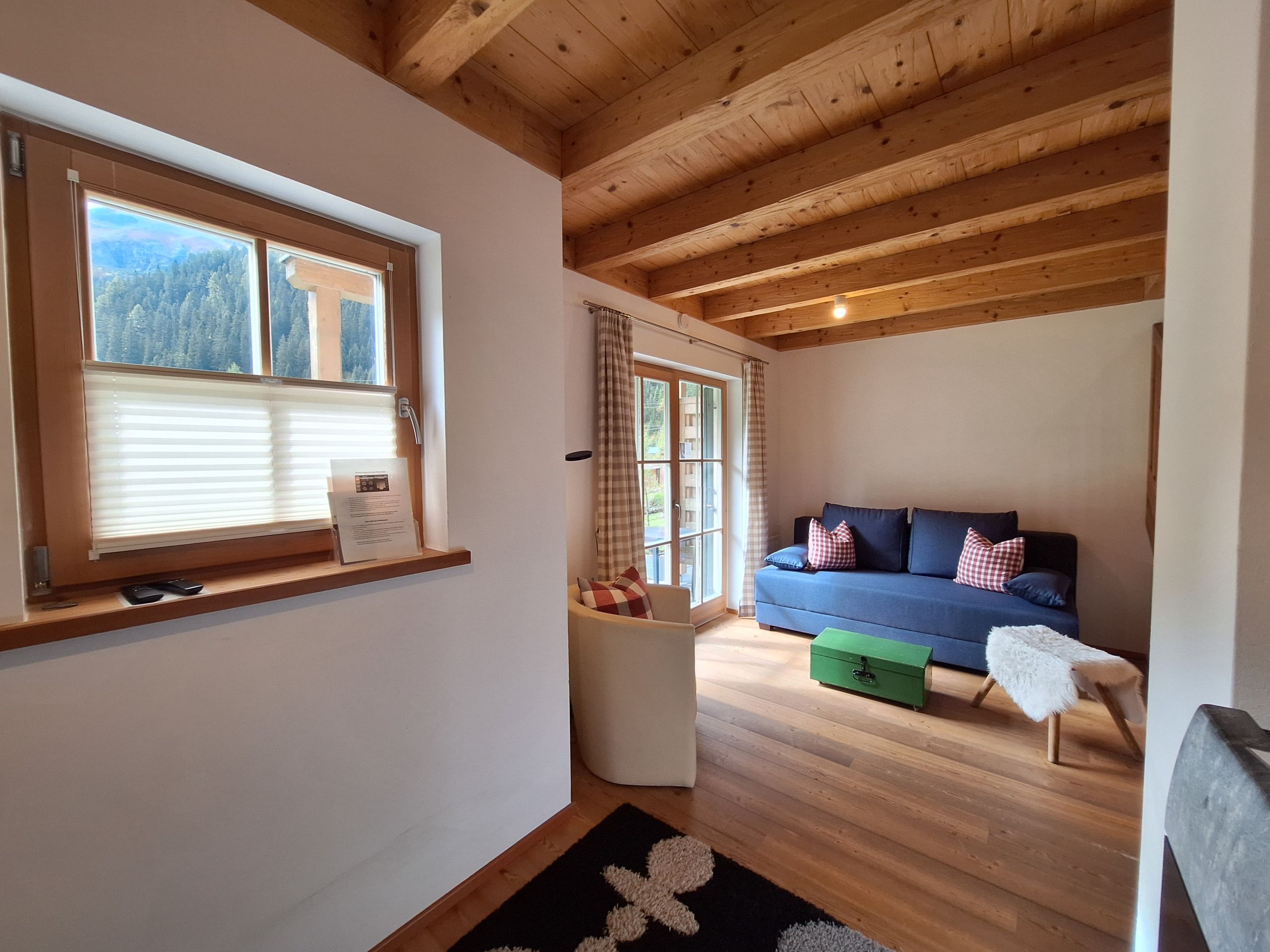 Une pièce avec un plafond en bois, un canapé bleu orné de coussins, une petite table blanche et une commode verte.
