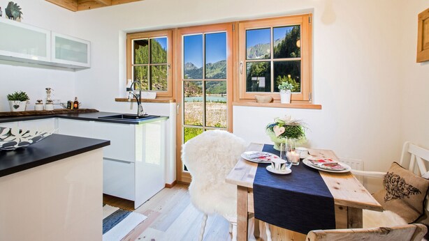 Una cocina moderna con armarios blancos, encimera negra y un amplio ventanal con vistas a la montaña.