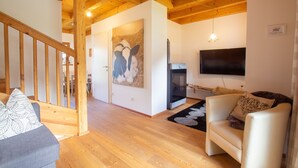 Amplia sala de estar con vigas de madera, chimenea, televisor de pantalla plana y sofá con cojines estampados.