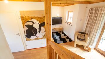 Una habitación con techo de madera, un televisor montado en la pared, un tapete pequeño, una silla y una ventana con cortina.