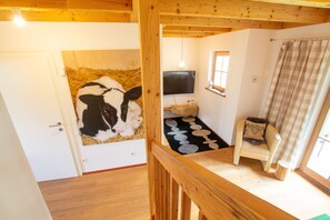 Une pièce avec un plafond en bois, un téléviseur fixé au mur, un petit tapis, une chaise et une fenêtre avec un rideau.