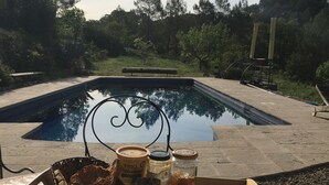 Une table placée au bord de la piscine, sur laquelle se trouvent un plateau avec du pain, des pots et un couteau.
