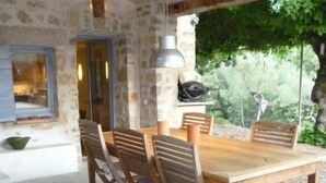 Une pièce aux murs de pierre, avec une grande table et des chaises en bois, un luminaire suspendu et une vue sur la verdure à l’extérieur.