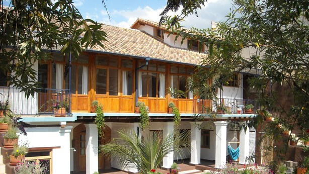 A two-story building with a tiled roof, wooden balconies, and a garden with various plants and flowers. - Maisonette apartment in historic Quito, with fantastic garden (Quito)