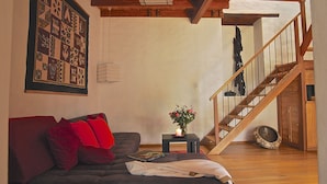 A cozy living room with a dark-colored sofa, a small table with a candle and flowers, and a wooden staircase. - Maisonette apartment in historic Quito, with fantastic garden (Quito)