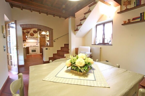 A dining area with a table set for two, a staircase leading to an upper level, and a kitchen in the background. - Nice little house near the beach with a nice garden. Air conditioning. (Pietrasanta)