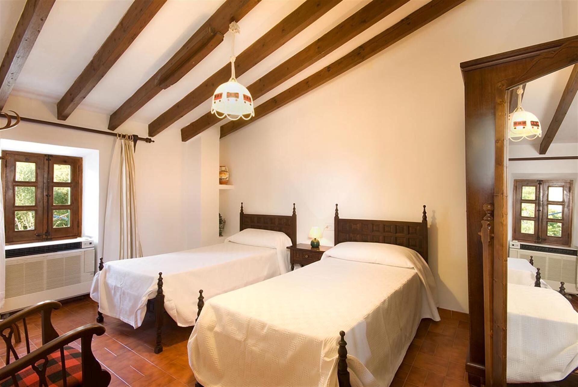 Una habitación con dos camas individuales, vigas de madera en el techo, una ventana con cortinas y un radiador.