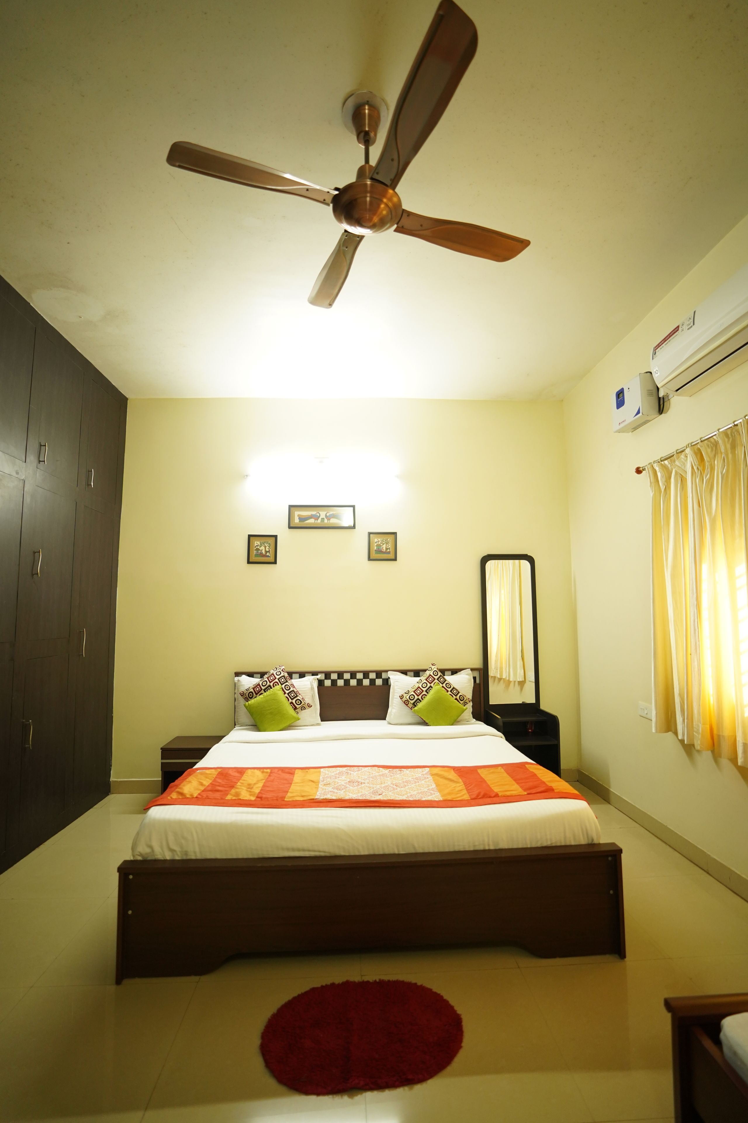 Quarto com cama, ventoinha no teto, espelho e janela com cortinas.