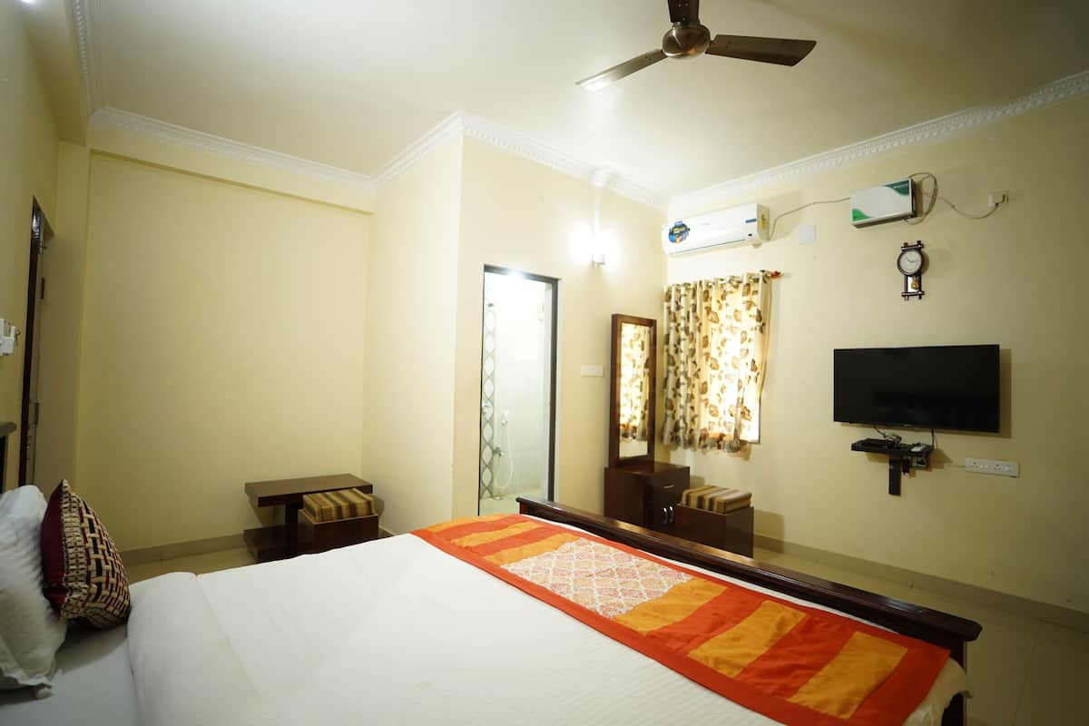 Una habitación de hotel con cama, ventilador de techo, televisor, espejo y ventana con cortinas.