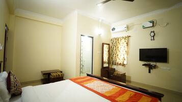 A hotel room with a bed, a ceiling fan, a television, a mirror, and a window with curtains.