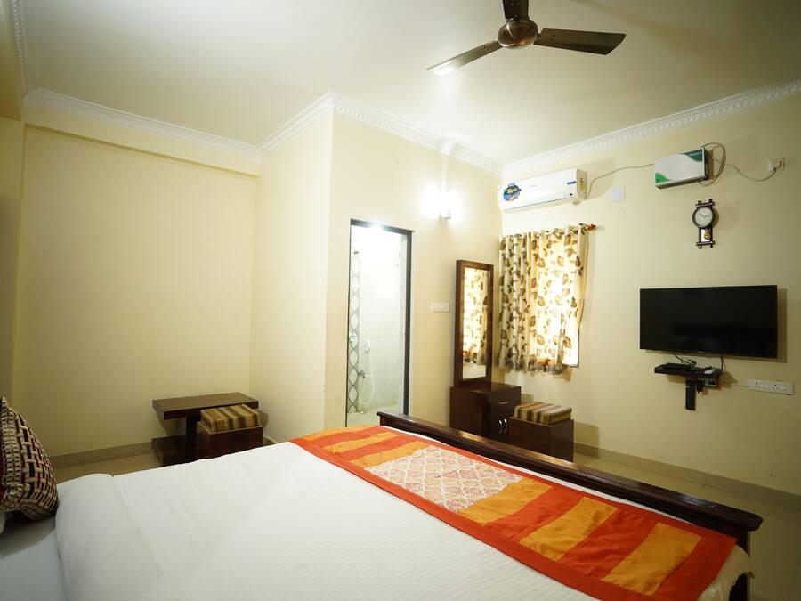 A hotel room with a bed, a ceiling fan, a television, a mirror, and a window with curtains.