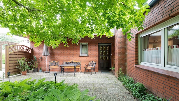 Casa de ladrillo con patio que incluye una mesa, sillas, un portón de madera y una ventana con cortinas.