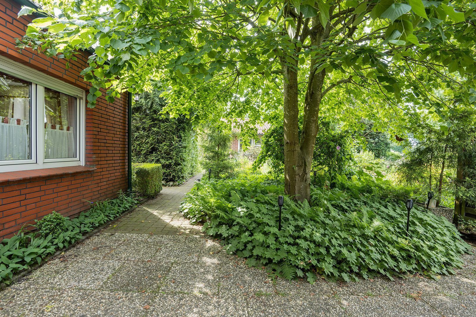 Een tuinpad dat leidt naar een bakstenen gebouw met een raam.