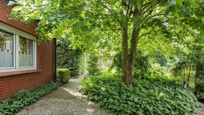 Un sendero en un jardín que lleva a un edificio de ladrillo con una ventana.