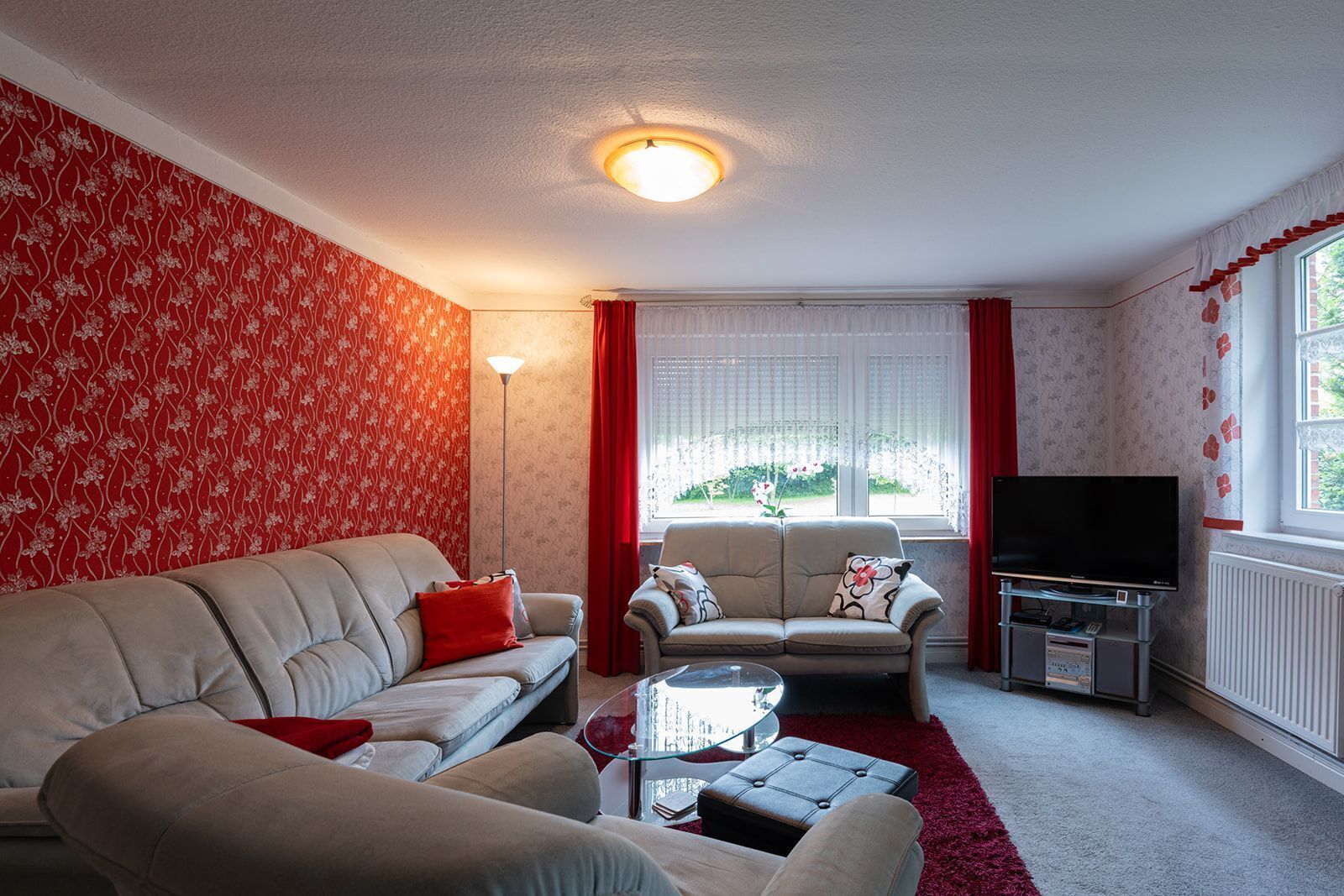 A living room with a sofa, a smaller couch, a glass coffee table, a television, and a radiator.