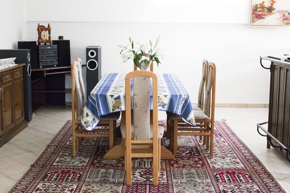 Un coin repas avec une table dressée pour quatre personnes, entourée de chaises, un vase décoratif avec des fleurs et un tapis à motifs.
