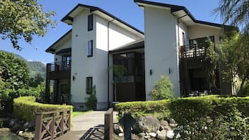 A modern two-story building with a white exterior, a wooden deck, and a landscaped garden with rocks and shrubs.