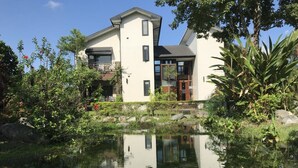 A modern two-story house with a pond in front, surrounded by lush greenery and trees. - Kanazawa House (Ji'an)