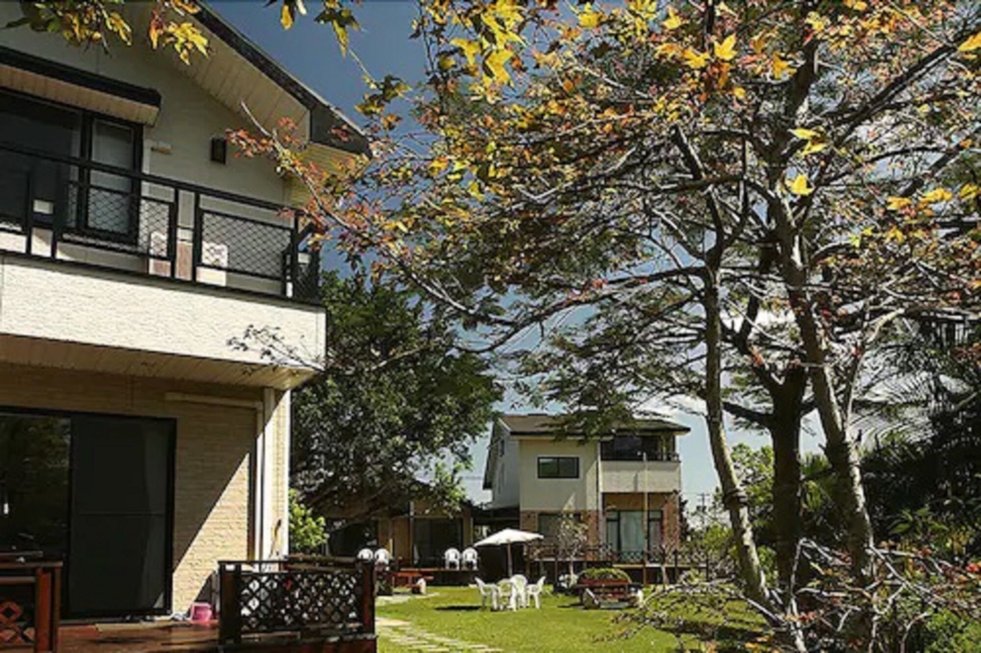 A two-story building with a balcony, a grassy yard, and a tree with yellow leaves.