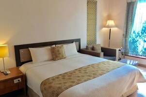 Una habitación de hotel con una cama grande, una mesita de noche con lámpara y un ventanal con vistas.