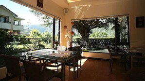A dining area with a large table and chairs, large windows offering a view of a garden and a building in the background. - Kanazawa House (Ji'an)