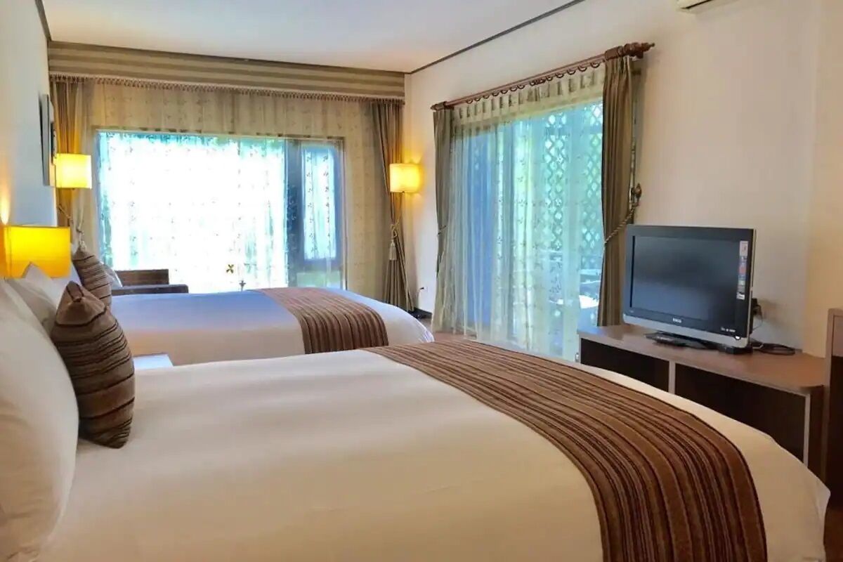 A hotel room with two beds, a television on a stand, and curtains on the windows.