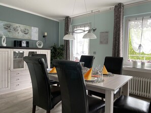 A dining area with a white table, black chairs, and a window with curtains. - Detached vacation home in a quiet cul-de-sac - dogs welcome - WiFi included (Bad Sachsa)