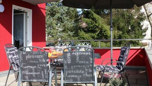 Une terrasse extérieure avec une table et des chaises, un bâtiment rouge et un grand parasol.