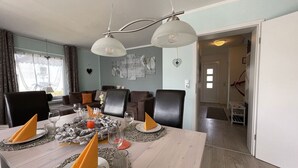 Un coin repas avec une table en bois dressée pour quatre personnes, deux lampes suspendues et une vue sur un salon comprenant un canapé et une table à manger.